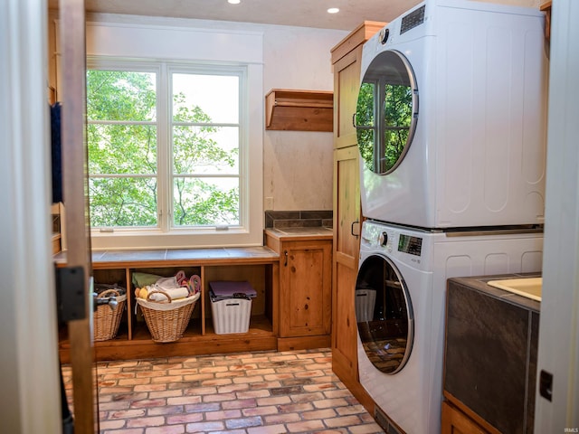 laundry room featuring stacked washer / drying machine, a healthy amount of sunlight, and cabinets