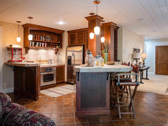 kitchen featuring appliances with stainless steel finishes, dark tile floors, a kitchen breakfast bar, kitchen peninsula, and pendant lighting