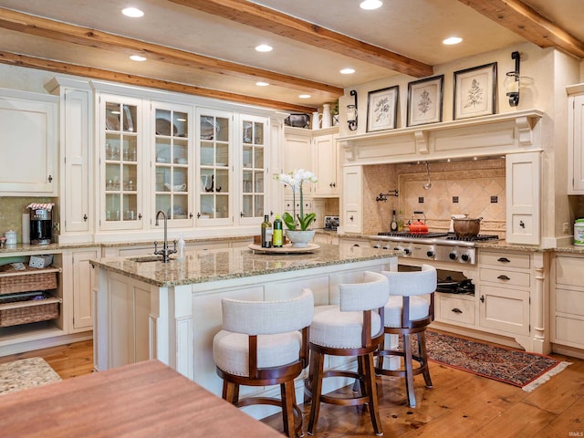 kitchen with beamed ceiling, light hardwood / wood-style floors, and a kitchen island with sink