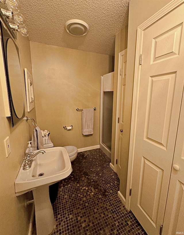 bathroom featuring a shower with shower door, toilet, tile floors, and a textured ceiling