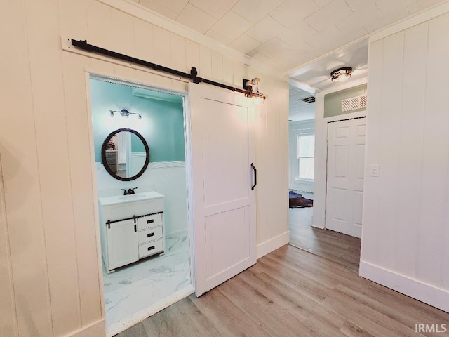 corridor with light hardwood / wood-style flooring, sink, and a barn door