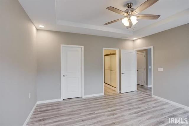 unfurnished bedroom with ceiling fan, a raised ceiling, and light hardwood / wood-style flooring