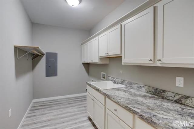 washroom with sink, electric panel, cabinets, washer hookup, and light hardwood / wood-style floors