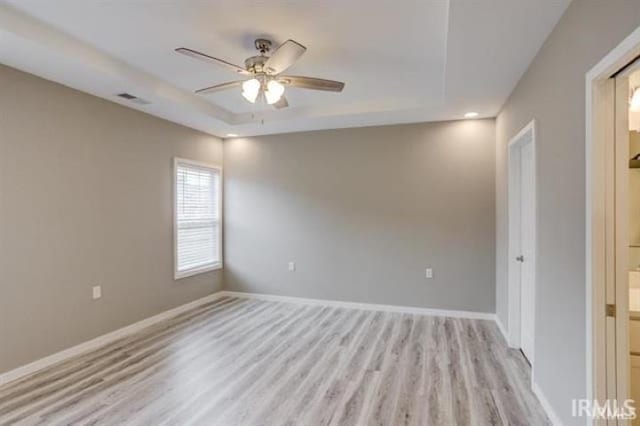 unfurnished room with light hardwood / wood-style flooring, a raised ceiling, and ceiling fan