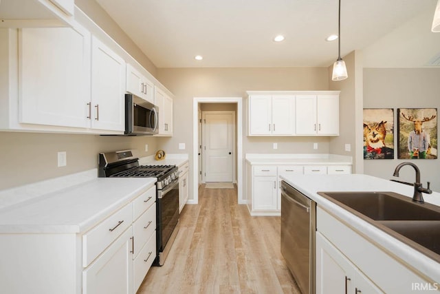 kitchen featuring appliances with stainless steel finishes, hanging light fixtures, white cabinetry, sink, and light wood-type flooring