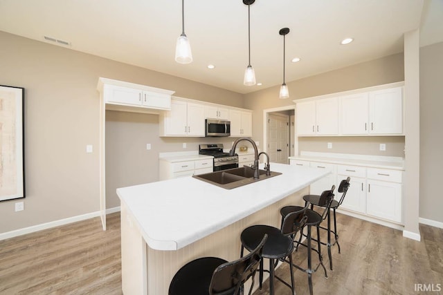 kitchen featuring appliances with stainless steel finishes, white cabinets, light hardwood / wood-style floors, and an island with sink