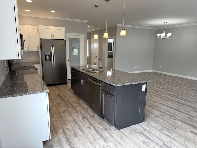 kitchen with decorative light fixtures, a sink, white cabinetry, appliances with stainless steel finishes, and a center island with sink