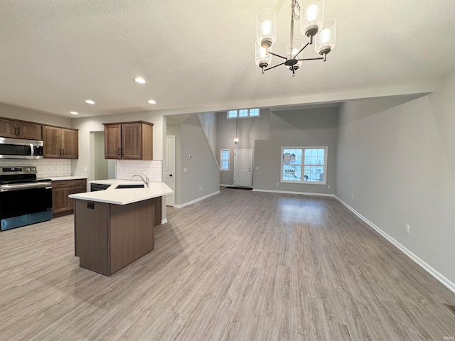 kitchen with decorative light fixtures, light wood-type flooring, kitchen peninsula, stainless steel appliances, and backsplash