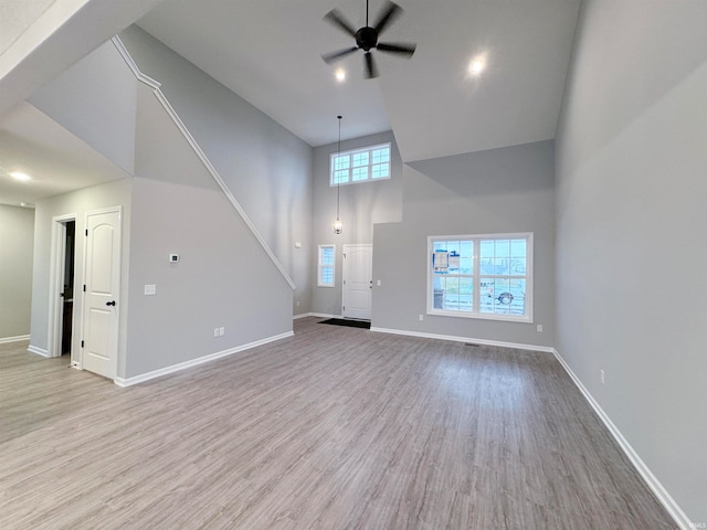 unfurnished living room with a towering ceiling, light hardwood / wood-style flooring, and ceiling fan