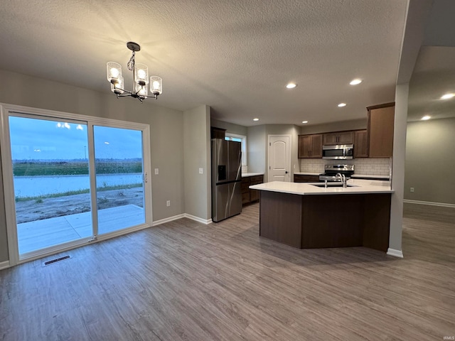 kitchen with hanging light fixtures, dark brown cabinets, stainless steel appliances, a water view, and wood-type flooring