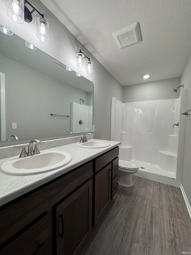 bathroom with wood-type flooring, vanity, walk in shower, toilet, and a textured ceiling