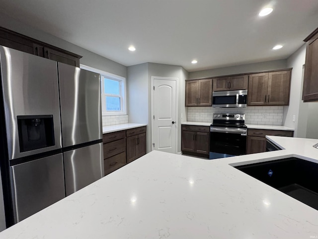 kitchen featuring light stone counters, dark brown cabinetry, and appliances with stainless steel finishes