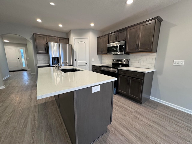 kitchen featuring tasteful backsplash, stainless steel appliances, a kitchen island with sink, sink, and light hardwood / wood-style floors