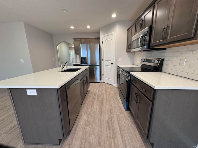 kitchen with dark brown cabinetry, stainless steel appliances, sink, light hardwood / wood-style floors, and an island with sink