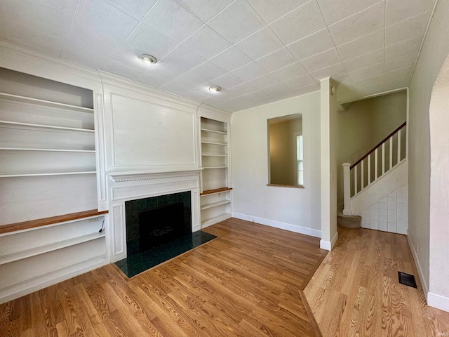 unfurnished living room with light hardwood / wood-style floors, a fireplace, and built in shelves