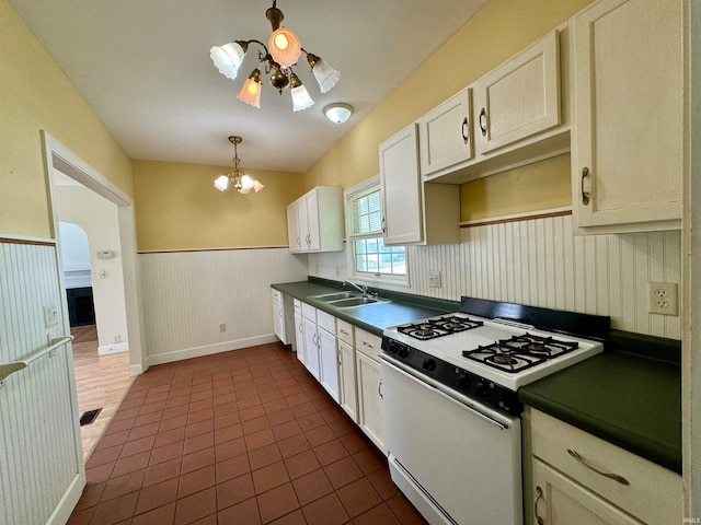 kitchen with white range with gas cooktop, dark tile floors, sink, ceiling fan with notable chandelier, and pendant lighting