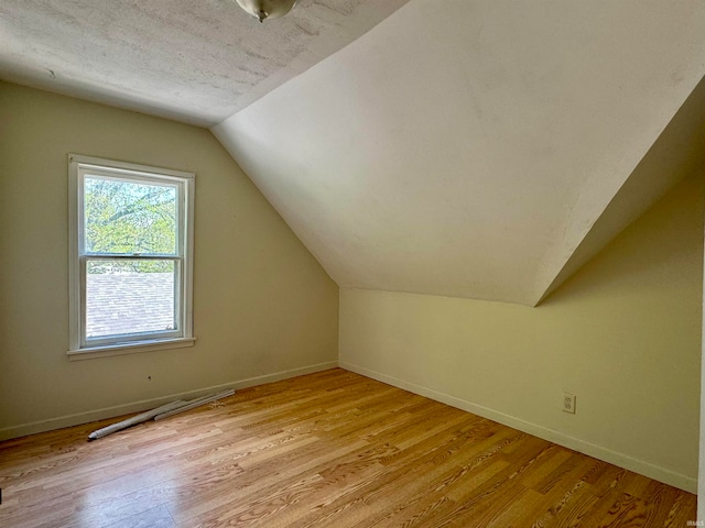 bonus room featuring a textured ceiling, vaulted ceiling, and light wood-type flooring