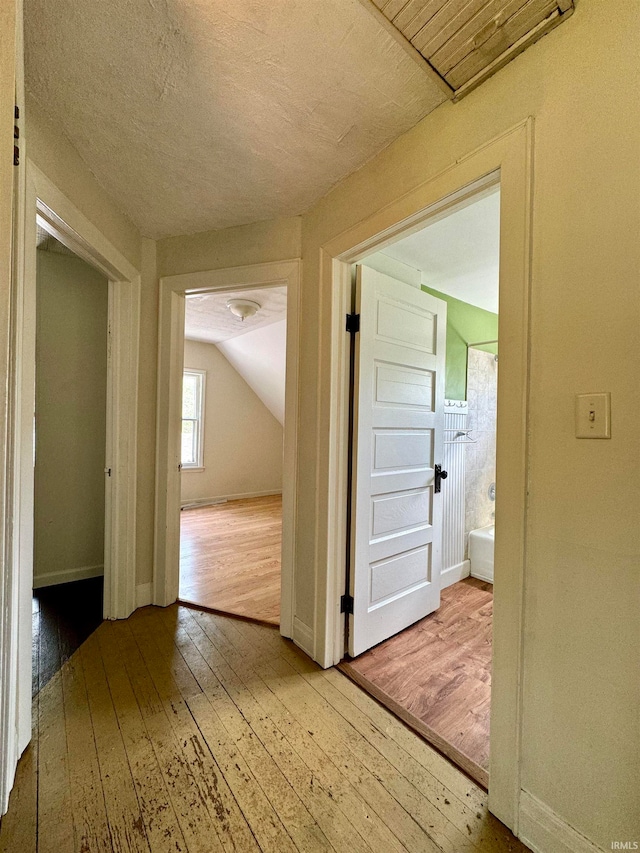 hallway with lofted ceiling, hardwood / wood-style floors, and a textured ceiling