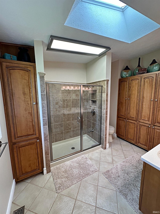 bathroom with a skylight, a shower with shower door, tile floors, and toilet