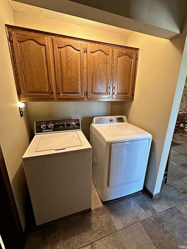 laundry area featuring cabinets, dark tile flooring, and washing machine and clothes dryer