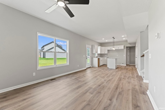 unfurnished living room featuring ceiling fan, light hardwood / wood-style flooring, a wealth of natural light, and sink