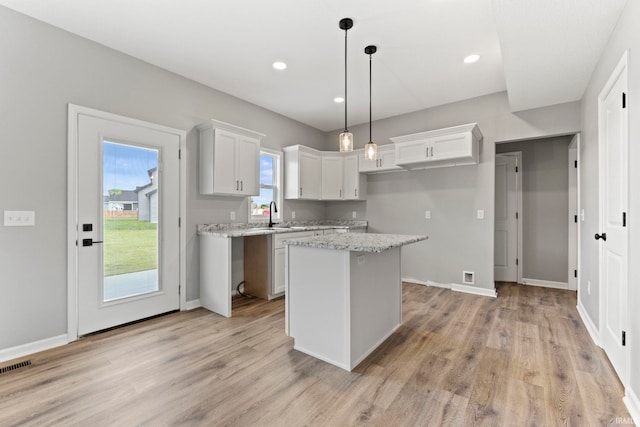 kitchen featuring white cabinets, a center island, light hardwood / wood-style flooring, and light stone countertops