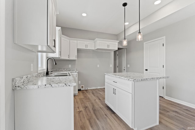 kitchen with decorative light fixtures, light hardwood / wood-style floors, a kitchen island, white cabinetry, and sink