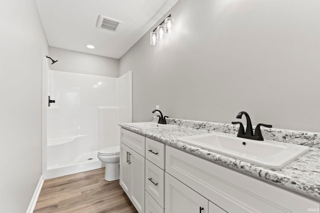 bathroom with double vanity, a textured ceiling, hardwood / wood-style floors, a shower, and toilet