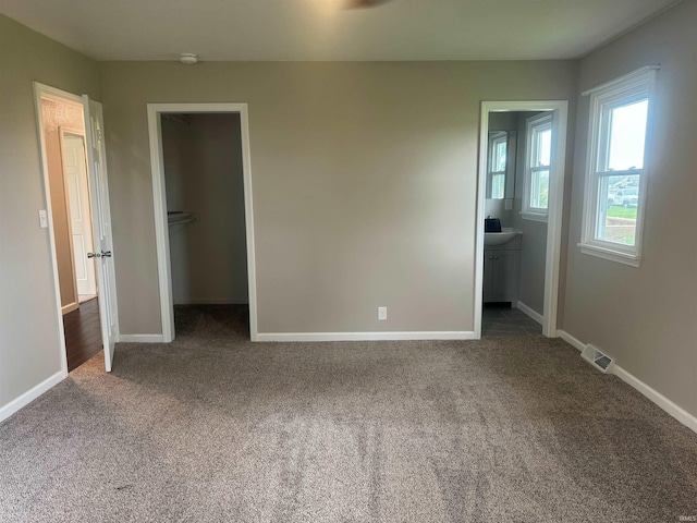 unfurnished bedroom featuring dark colored carpet, a closet, a spacious closet, and ensuite bathroom