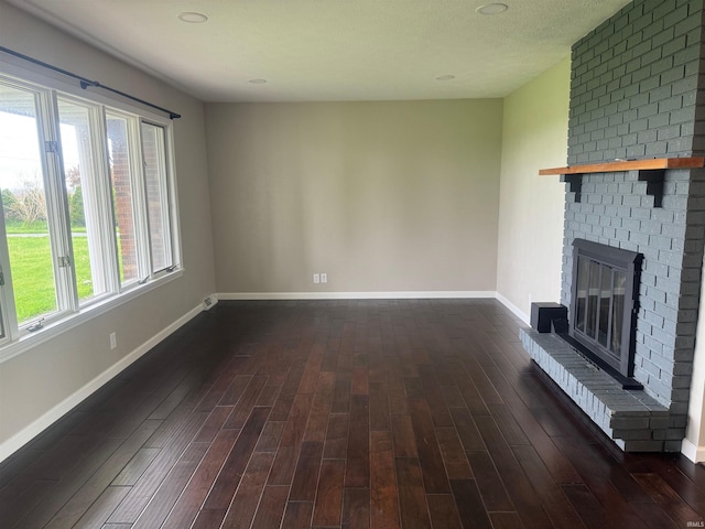 unfurnished living room featuring brick wall, dark hardwood / wood-style floors, a textured ceiling, and a fireplace