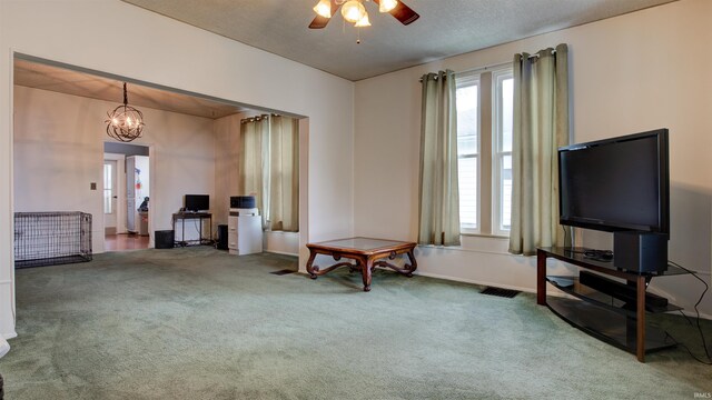 sitting room featuring ceiling fan with notable chandelier, dark carpet, and a textured ceiling