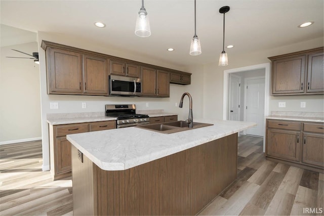 kitchen with hanging light fixtures, hardwood / wood-style floors, sink, a center island with sink, and appliances with stainless steel finishes