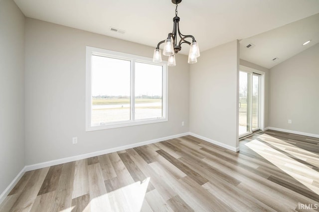 spare room with an inviting chandelier, vaulted ceiling, and light hardwood / wood-style floors