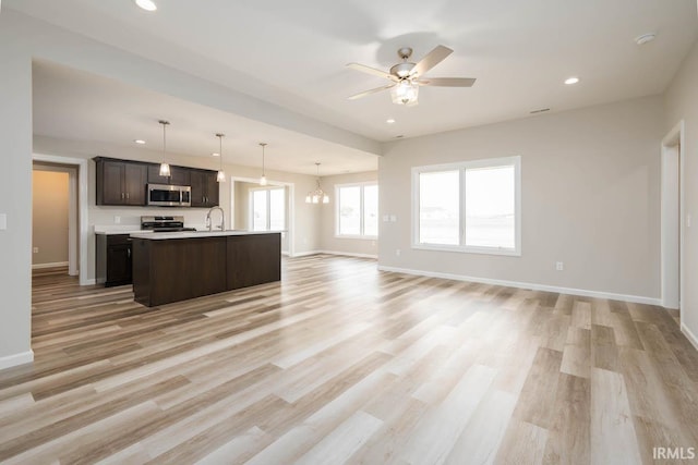 kitchen featuring hanging light fixtures, a kitchen island with sink, range, light wood-type flooring, and dark brown cabinetry