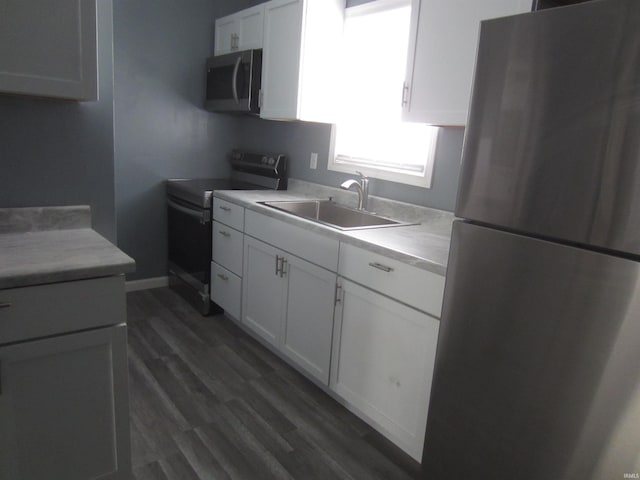 kitchen with appliances with stainless steel finishes, dark hardwood / wood-style flooring, white cabinetry, and sink