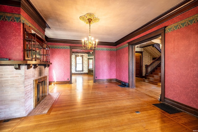 unfurnished dining area featuring a fireplace, crown molding, light wood-type flooring, and a chandelier