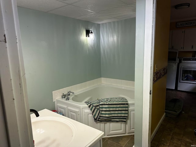 bathroom featuring a washtub, a drop ceiling, washing machine and dryer, and vanity