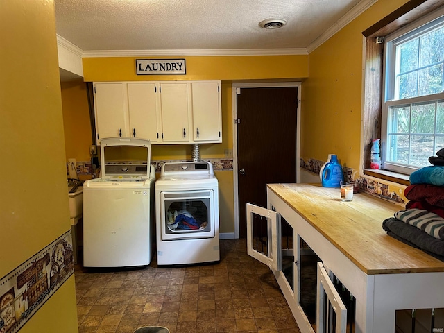 clothes washing area featuring cabinets, a textured ceiling, washing machine and dryer, and plenty of natural light