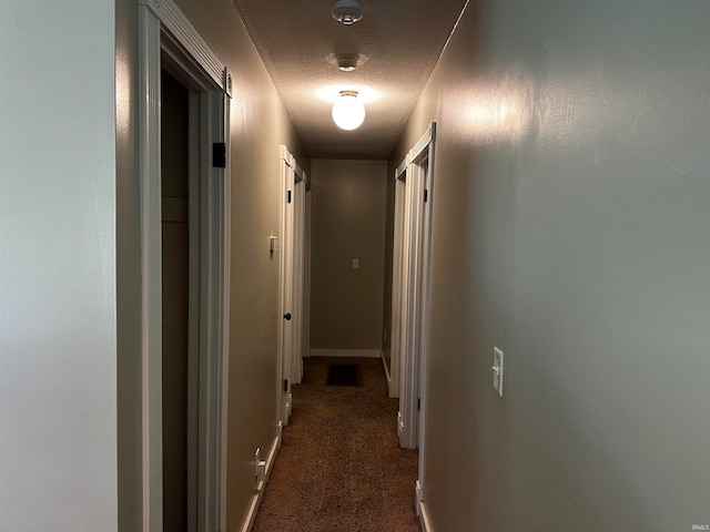 hallway featuring dark colored carpet and a textured ceiling