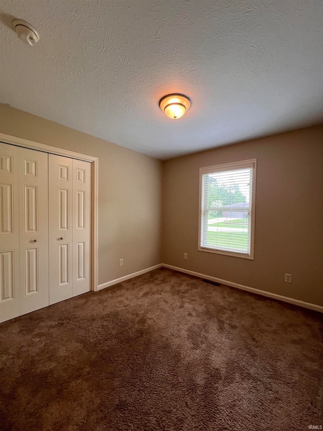 unfurnished bedroom featuring a textured ceiling and dark colored carpet