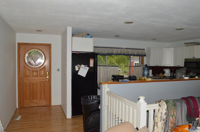 kitchen featuring black refrigerator with ice dispenser, light wood-type flooring, stove, and white cabinetry