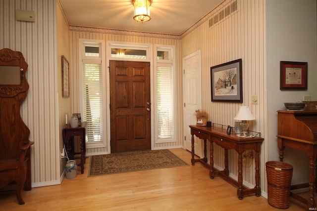 entrance foyer featuring light hardwood / wood-style floors, ornamental molding, and a wealth of natural light