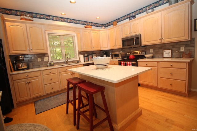 kitchen with stainless steel appliances, sink, light brown cabinets, light hardwood / wood-style floors, and a kitchen island