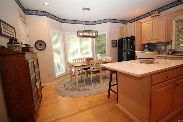 kitchen featuring decorative backsplash, black fridge, light hardwood / wood-style floors, a kitchen island, and hanging light fixtures