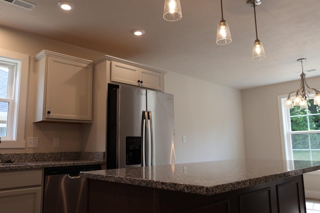 kitchen with pendant lighting, a notable chandelier, stainless steel appliances, white cabinetry, and dark stone counters