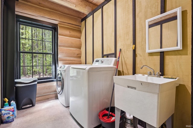 clothes washing area with sink, a healthy amount of sunlight, washing machine and clothes dryer, and rustic walls