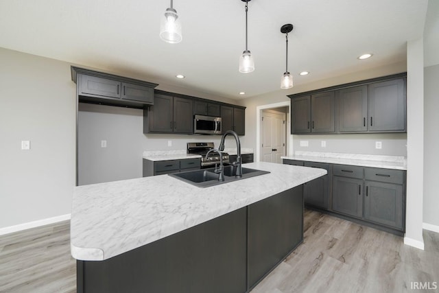 kitchen featuring hanging light fixtures, stainless steel appliances, light wood-type flooring, a center island with sink, and sink