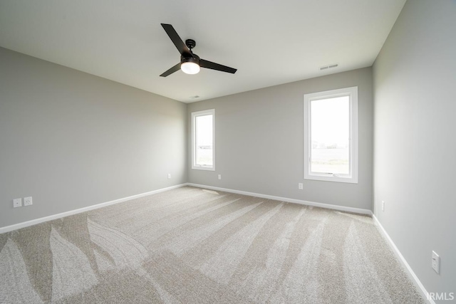 spare room featuring ceiling fan, light colored carpet, and a wealth of natural light