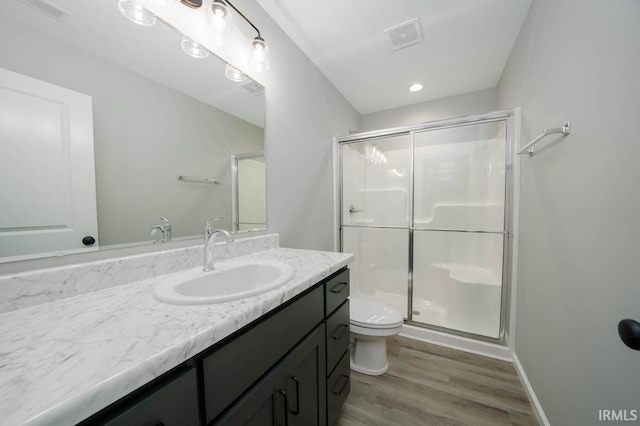 bathroom with hardwood / wood-style floors, vanity, toilet, and a shower with shower door