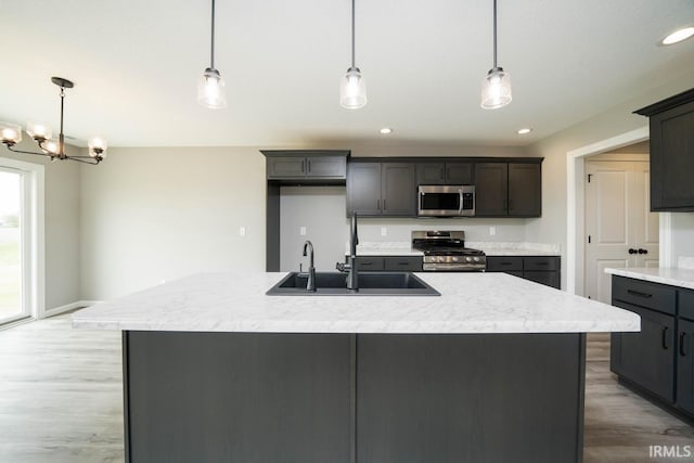 kitchen with pendant lighting, sink, an inviting chandelier, stainless steel appliances, and a center island with sink